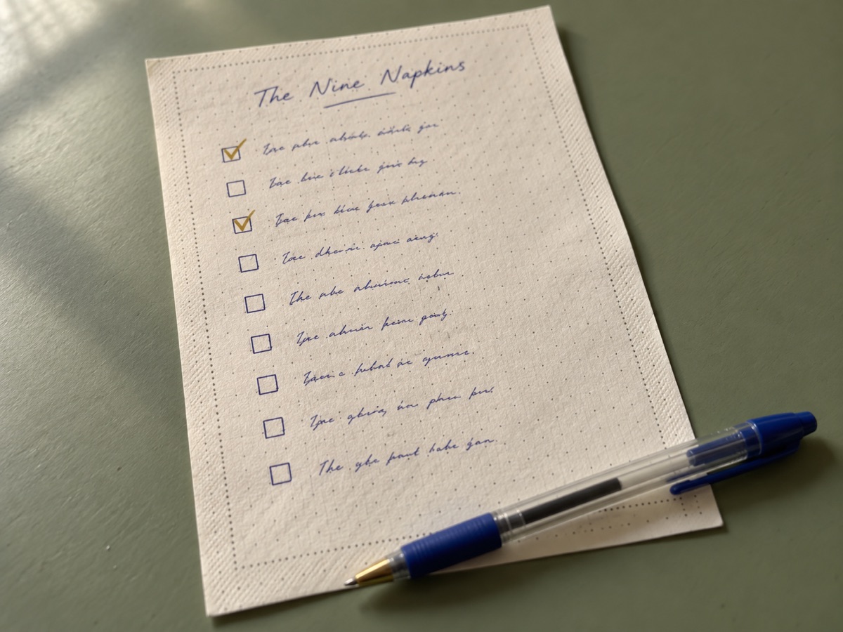 The Nine Napkins, a one-page checklist printed like a napkin, nine lines with a box beside each, two of them ticked, a blue pen across the corner.